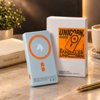 A light blue portable power bank with an orange circular logo stands in front of its white product box on a marble desk. The box features an orange and black 'Unicorn Report' logo and reads 'Pandaler Unicorn'.