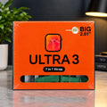 Orange retail box for a 7-in-1 watch strap, labeled ULTRA 3 and BIG 2.01", shown on a tabletop with a plant and lamp in the background.