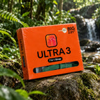 An orange retail box for a smartwatch strap labeled ULTRA 3 and BIG 2.01" is placed on a mossy rock outdoors in a forest setting with green foliage and a waterfall in the background.
