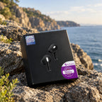 Black wireless earbud box with a pair of black and white earbuds printed on the front, placed on rocky coastal ground with the sea and cliffs blurred in the background. Purple Redington badges are visible on the box.