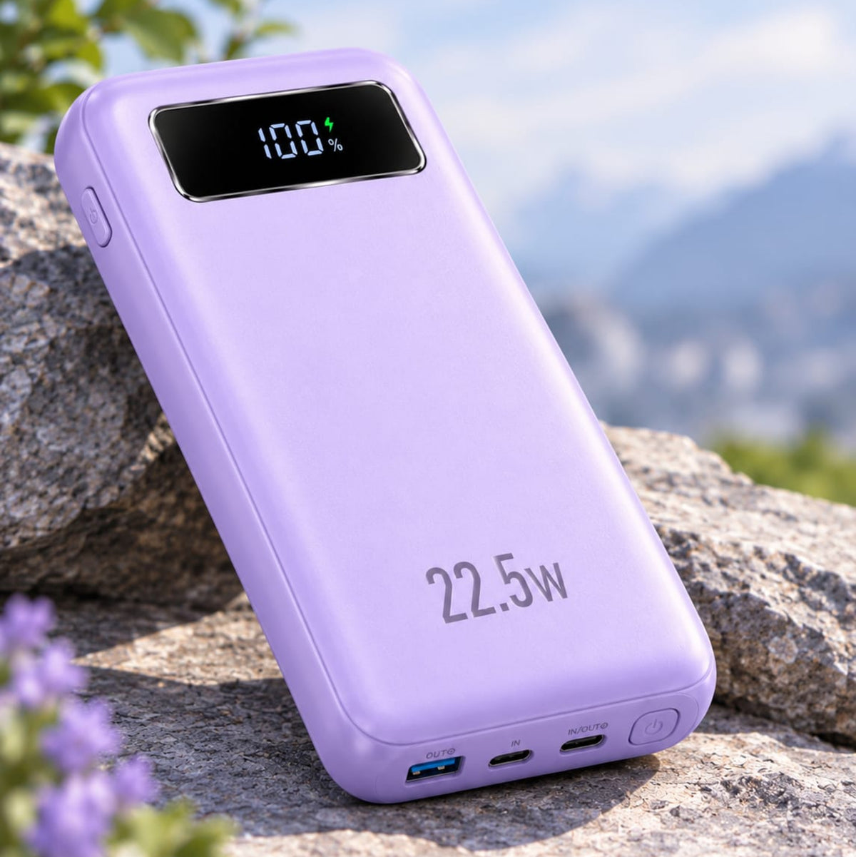 A light purple 22.5W portable power bank with a digital battery percentage display, resting on a large gray rock with a blurred outdoor background of green foliage and blue sky.