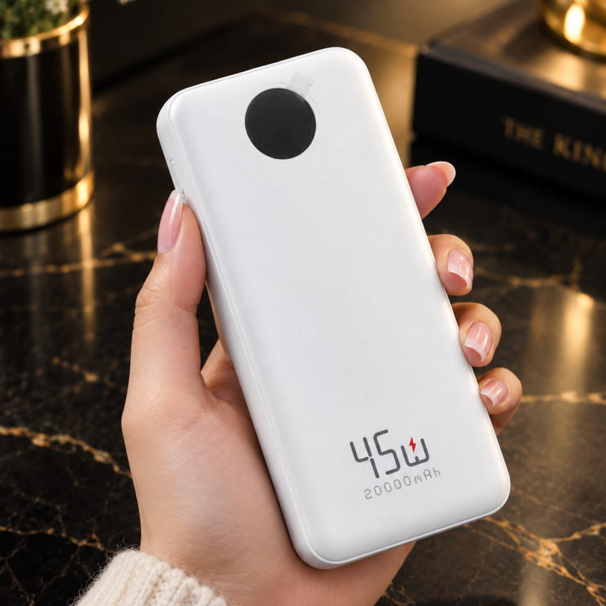 A hand holding a white 45W 20000mAh portable power bank with a circular camera-style cutout on the back, set against a dark marble tabletop background.