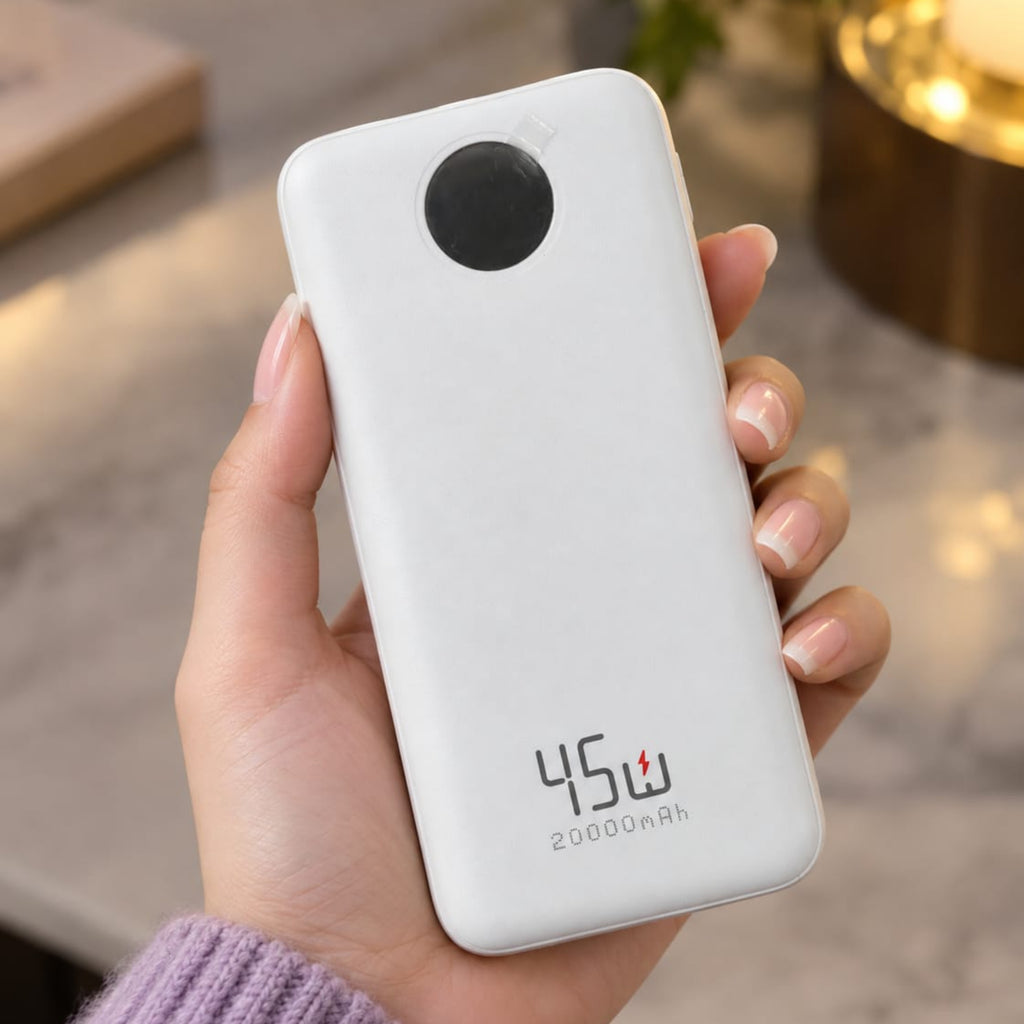 A hand holding a white portable power bank with a black circular camera cutout and the text '45W 20000mAh' printed on the back, set against a softly blurred indoor background.