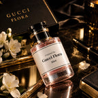 A bottle of Gucci Flora perfume with a black cap and white label, styled on a reflective dark marble surface with white flowers, a black Gucci Flora box, and gold-toned accessories.